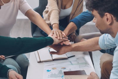 Close-up top view of modern business team keeping hands clasped while sitting in the office together