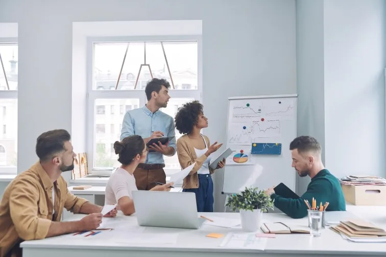 Group of confident young people in smart casual wear discussing business while having meeting in office