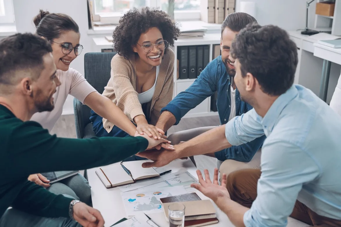 Confident young business team keeping hands clasped and smiling while sitting in the office together