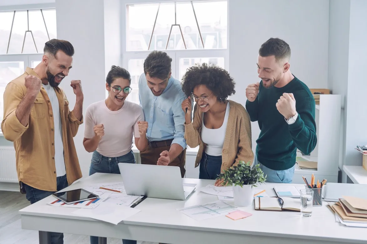 Group of happy young people in smart casual wear looking at laptop and gesturing while having meeting in the office